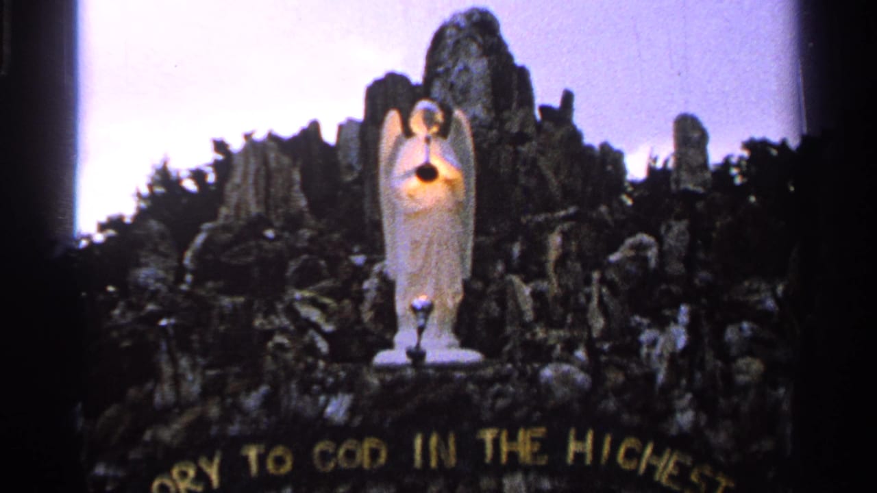 1965 Saint Louis 8mm frame with a handheld view of the angel sculpture, glowing light, and curved gold religious lettering.