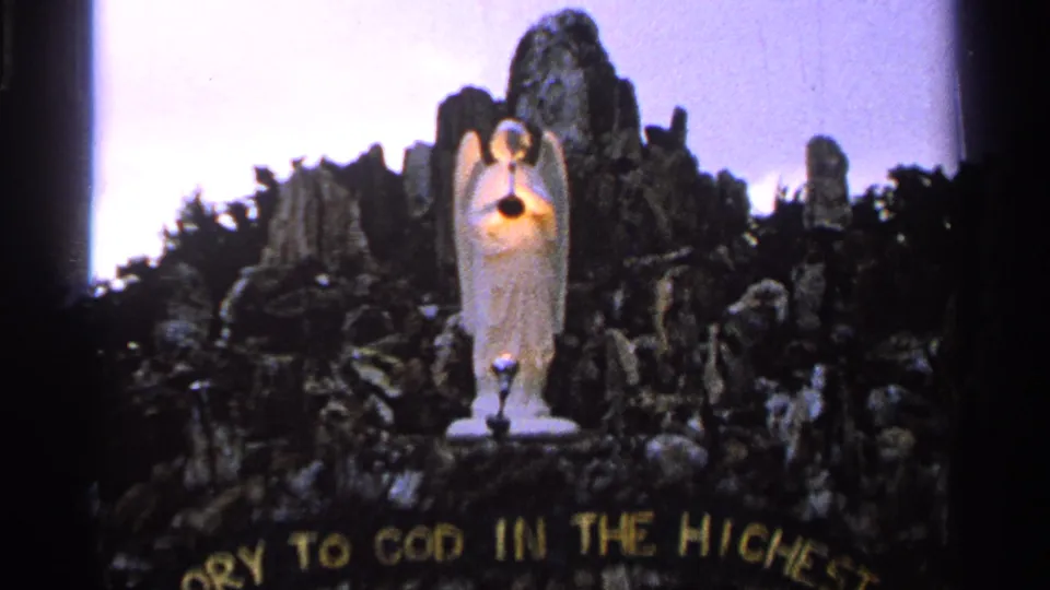 1965 Saint Louis 8mm frame with a handheld view of the angel sculpture, glowing light, and curved gold religious lettering.