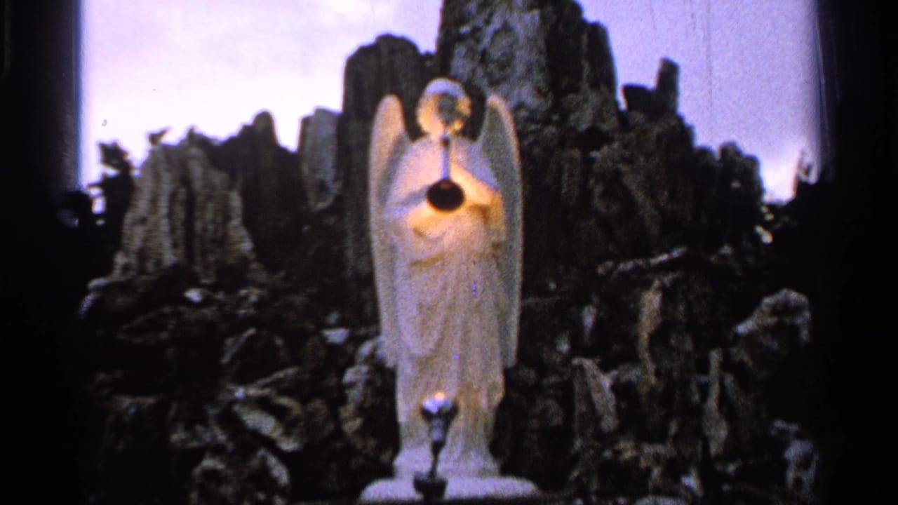 1965 Saint Louis home-movie frame with a closer view of the white angel sculpture and bright light against a dark rocky setting.