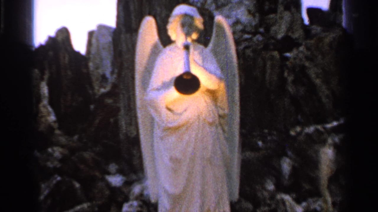 White angel statue with wings holds a horn in a dim garden display.