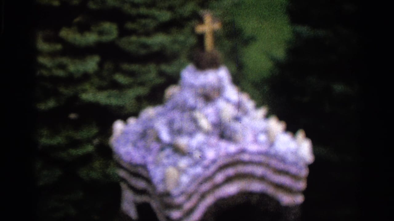Flower-covered cross or shrine form against dark greenery.