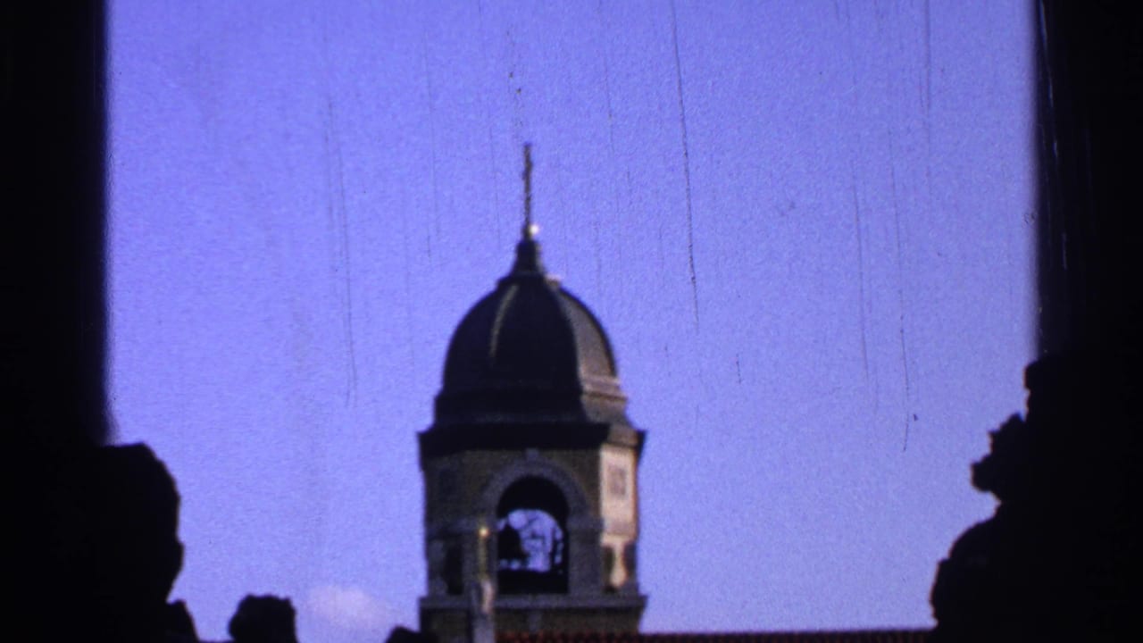 1965 Saint Louis frame centering a domed bell tower with an arched opening, blue sky, and dark edge silhouettes.