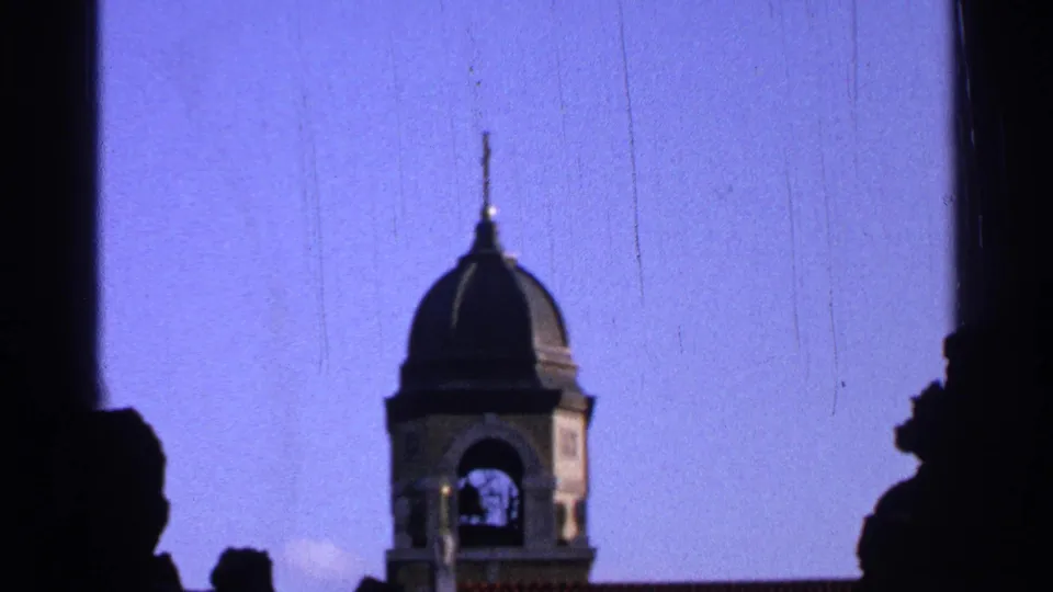 1965 Saint Louis frame centering a domed bell tower with an arched opening, blue sky, and dark edge silhouettes.