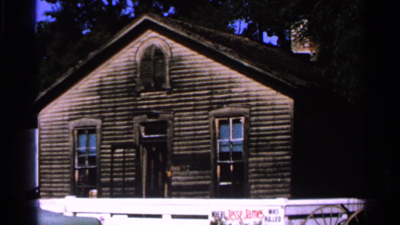 Weathered gabled wooden building with arched upper window and front porch rail.