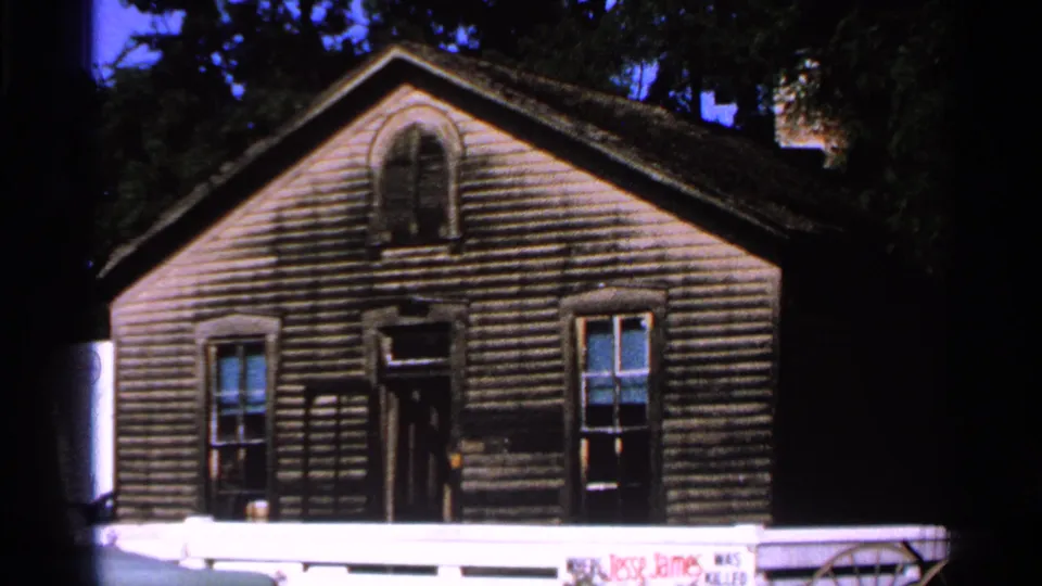 Closer 1965 view of the Jesse James Home exterior, showing wood siding, front windows, a dark doorway, and a low white railing.