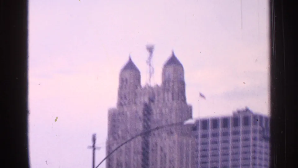 Soft-focus Saint Louis skyline view with a twin-towered building, traffic mast, and neighboring high-rise in faded 8mm color.