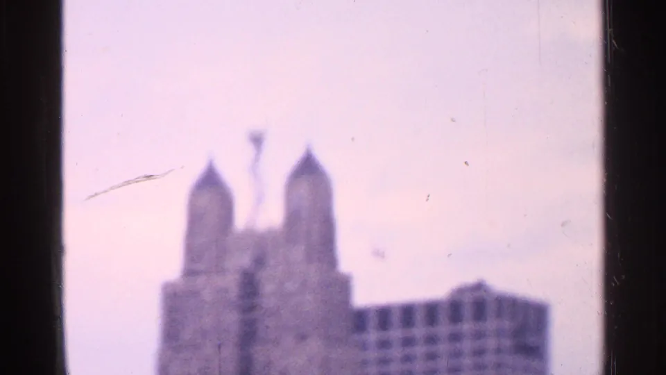Soft 1965 8mm frame showing a distant twin-spired Missouri landmark with pale sky and visible film edges.