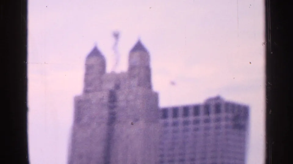 Soft 8mm view of a twin-spired landmark with an adjoining windowed building, framed by dark film edges.