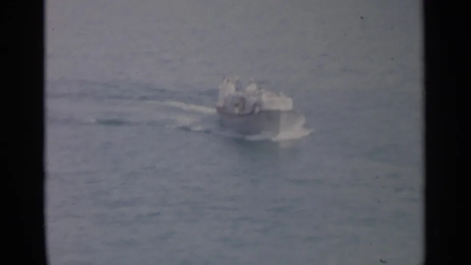 Soft 8mm frame of a small motorboat on open water, with distant occupants and a pale wake behind it.