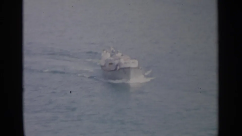 Small motorboat continues across the sea in soft 8mm footage, with distant people visible aboard.