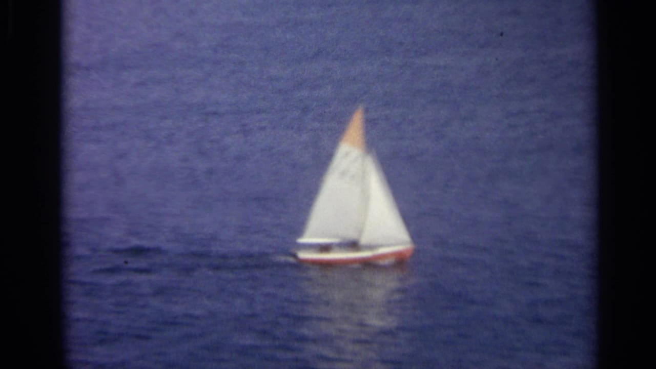 White sailboat with an orange sail tip on dark blue water.