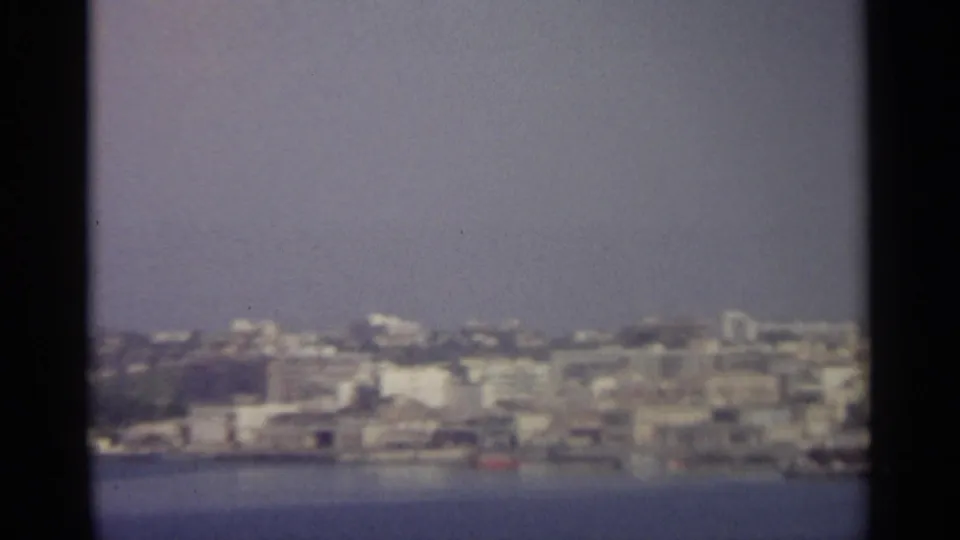 Distant Sicilian waterfront and hillside buildings appear slightly out of focus beyond a calm blue sea.
