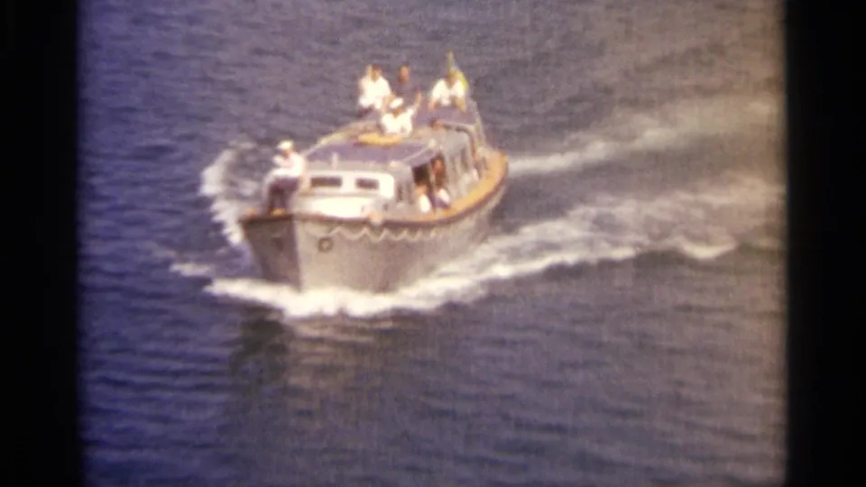 A small passenger motorboat passes through sunlit water with visible figures on deck and a foamy wake behind it.