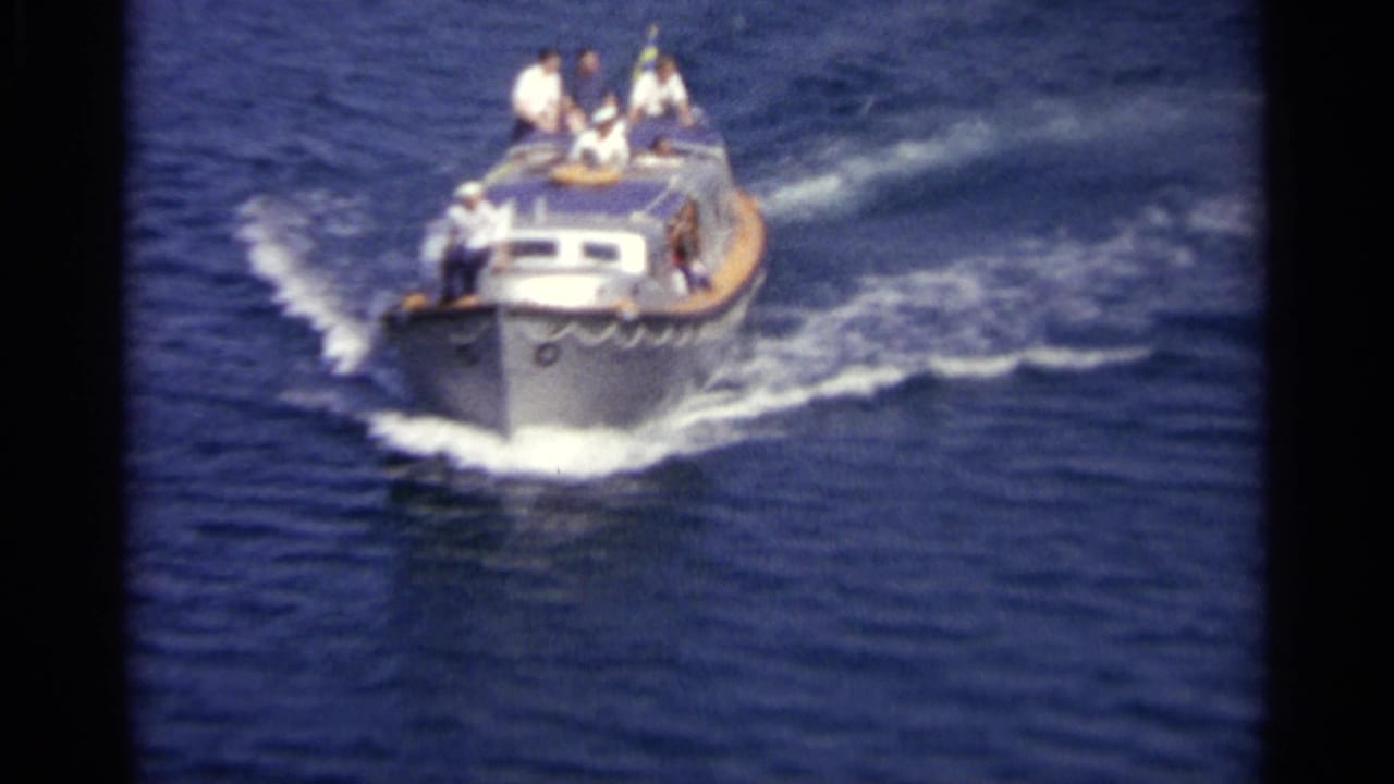 A small motorboat with several passengers travels over deep blue water in archival 8mm footage dated to 1965.