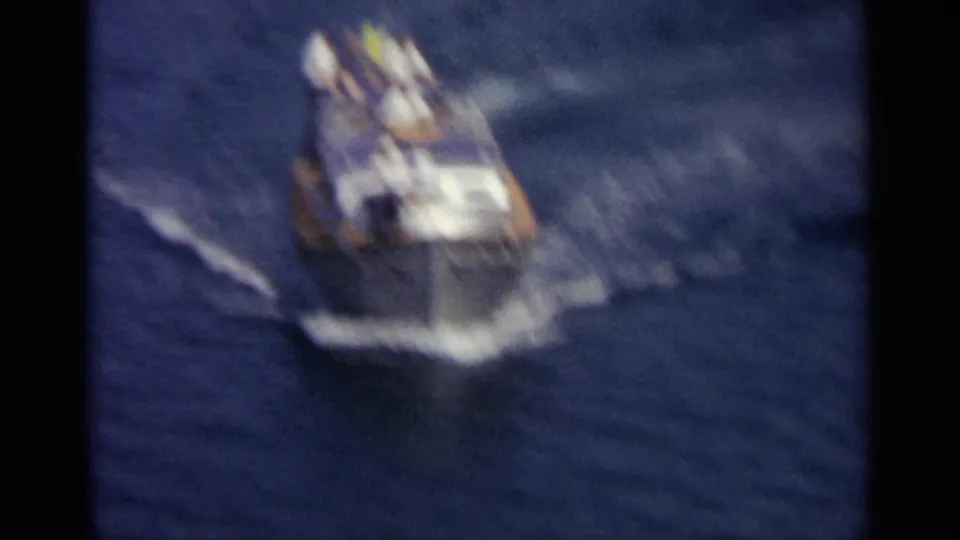 The motorboat appears blurred in motion as it turns across blue water, with passengers visible aboard.