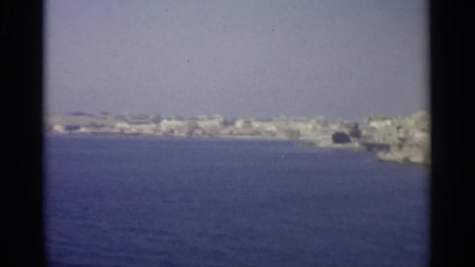 The coastal view continues, showing pale buildings along the shoreline beyond open blue water.