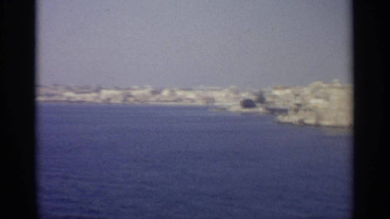 Distant pale coastal town across blue water with dark film borders.