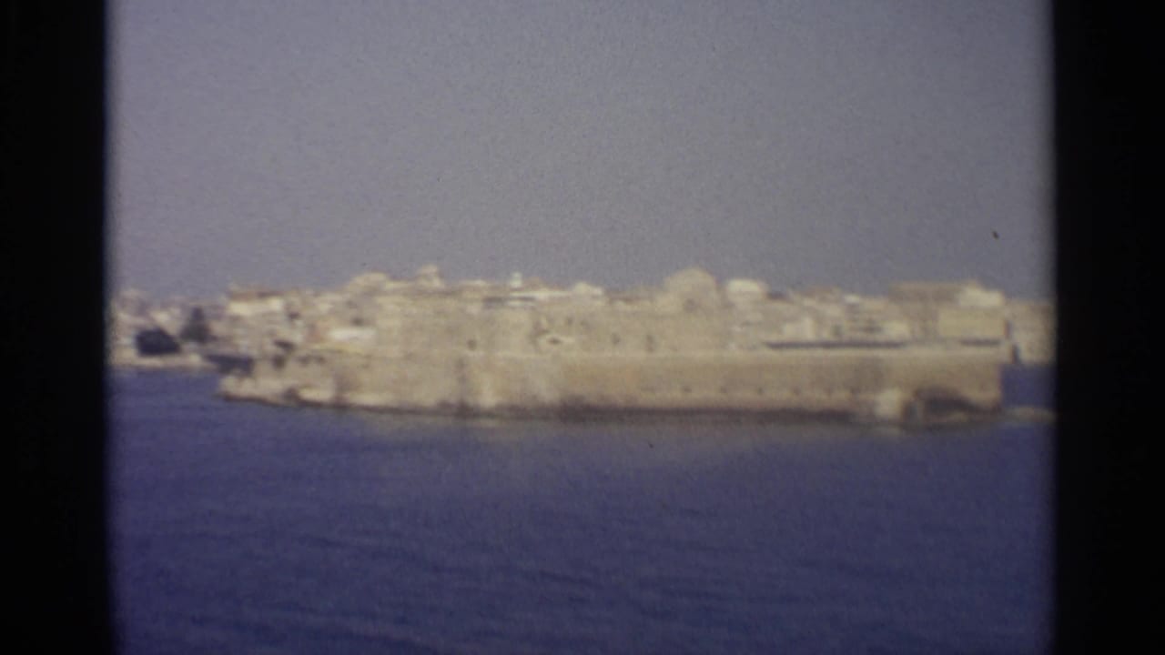 Distant fortified waterfront and pale buildings across blue water.
