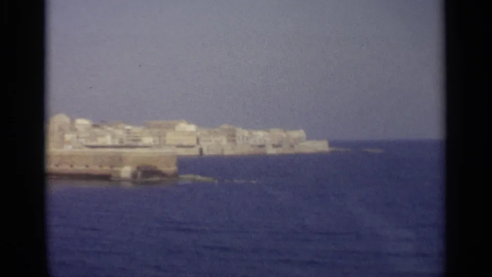 Final frame of the coastal panorama, with pale buildings and waterfront stonework receding toward open blue sea.