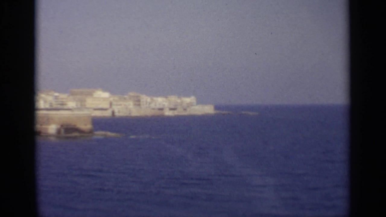 Distant white coastal buildings across blue sea under a pale sky.