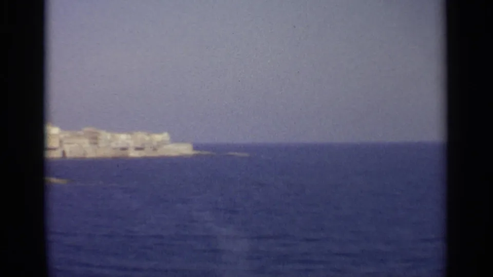 A soft 8mm frame shows Sicily's distant coast receding across open blue water beneath a pale horizon.