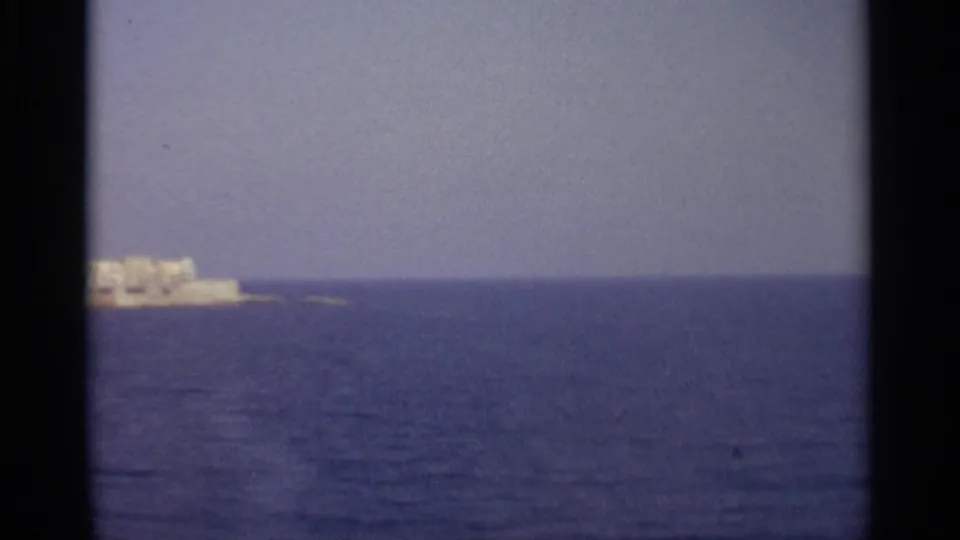 The 1965 home-movie view leaves only a small portion of the Sicilian shoreline at the left edge over blue water.