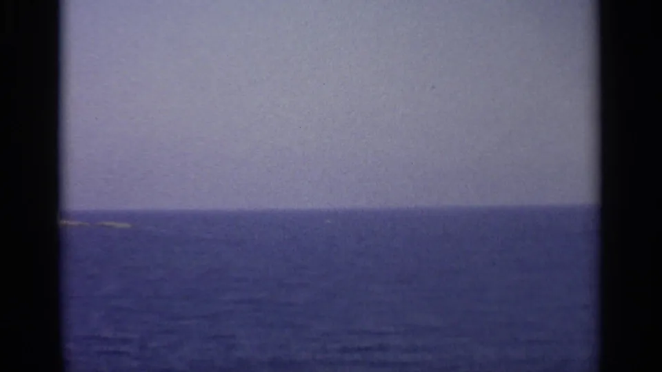 The final 8mm frame is mostly open Mediterranean water and pale sky, with a faint low shoreline near the left edge.