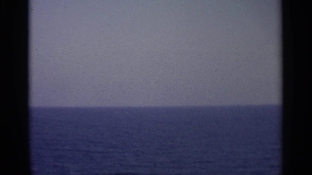 A soft 8mm view across open water and a pale horizon, filmed from a moving vessel with no people visible.