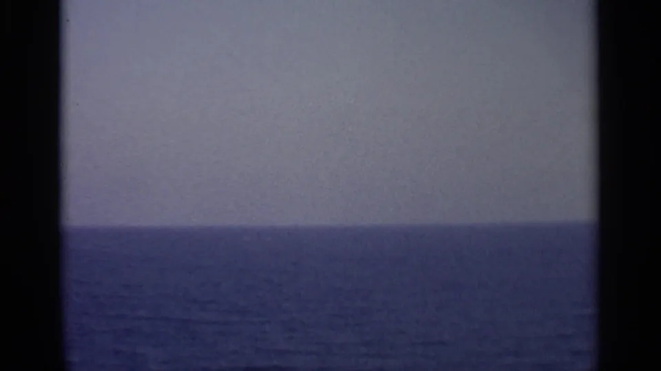 A soft 8mm view across open water and a pale horizon, filmed from a moving vessel with no people visible.