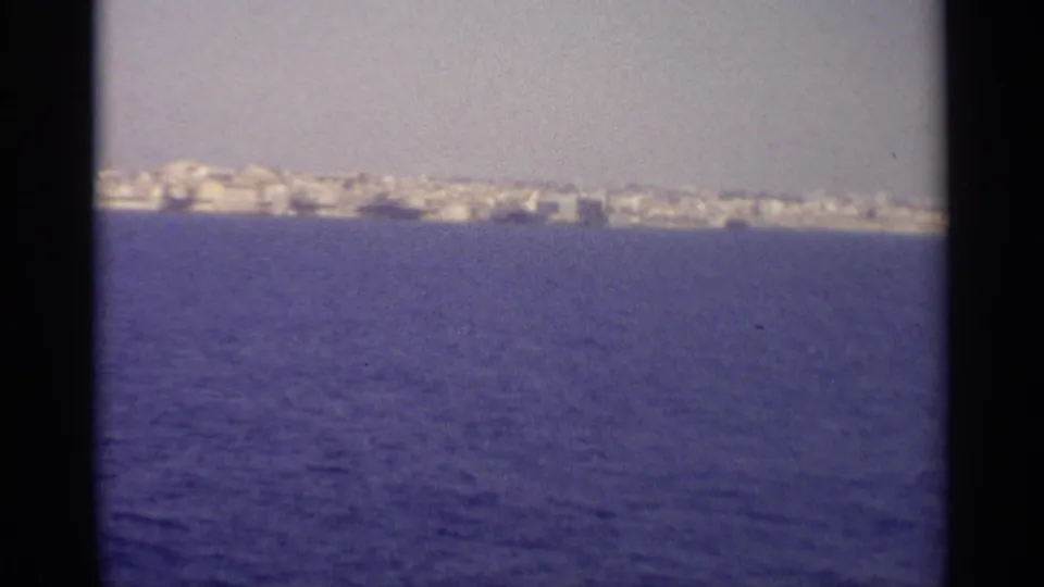 The boat view holds on a distant Sicilian coastal town, with blue sea filling most of the 8mm frame.