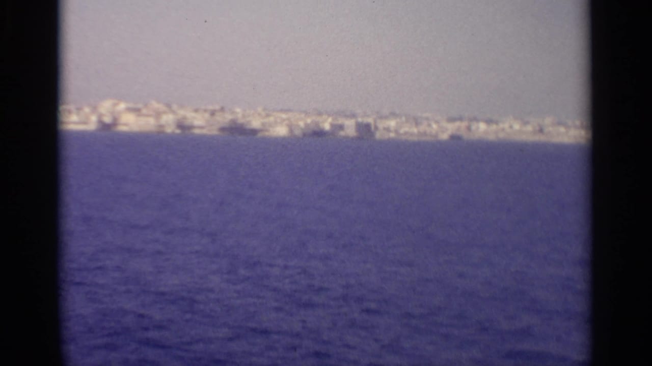 Distant white coastal buildings across blue water under a hazy sky.