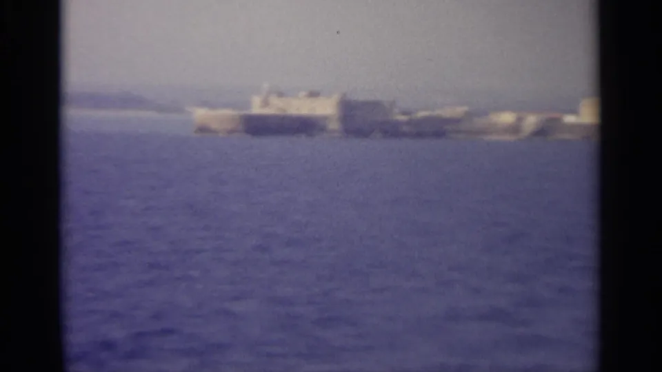 Soft 8mm frame showing a hazy coastal shoreline and low buildings across a wide blue bay.