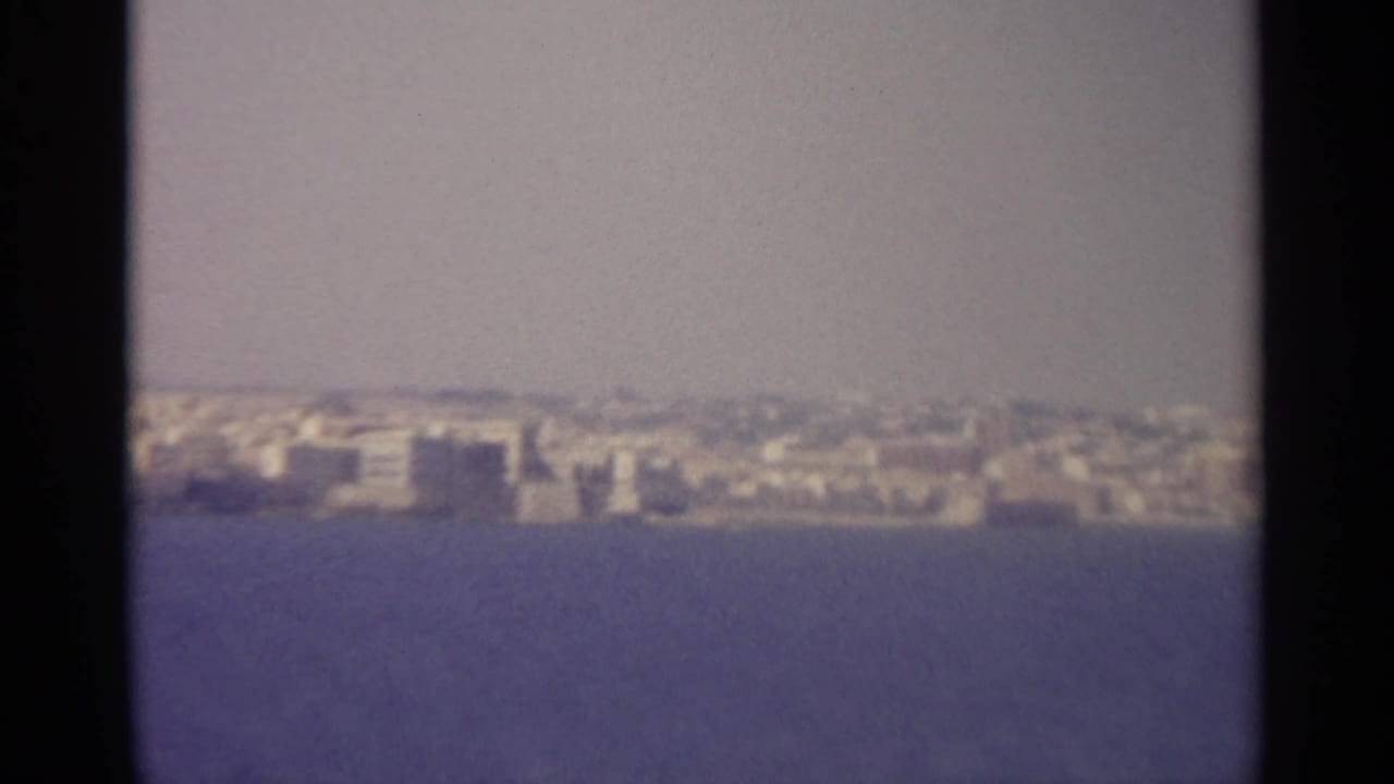 Distant coastal city across calm blue water under a pale hazy sky.