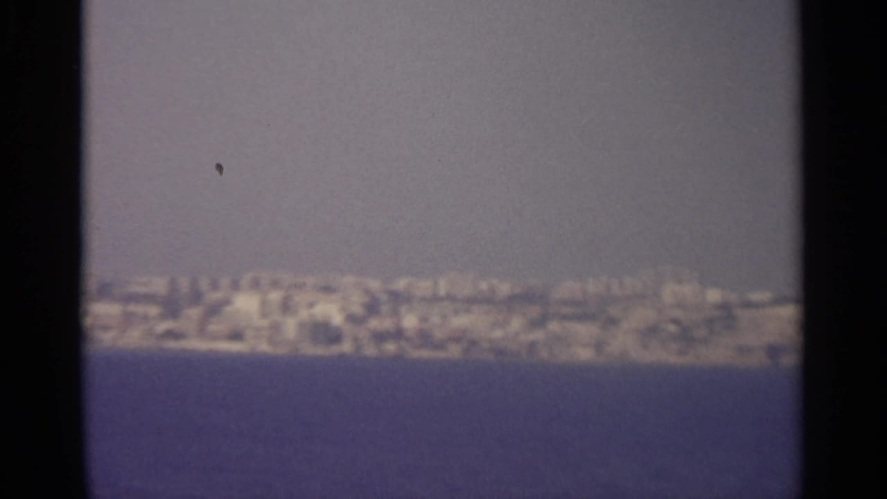 Distant hazy shoreline across blue water, framed by dark film borders.