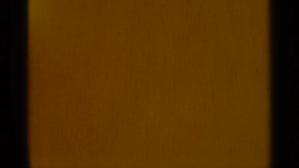 Warm amber-brown 8mm frame with dark side borders and visible film texture during an exposure or transition moment.