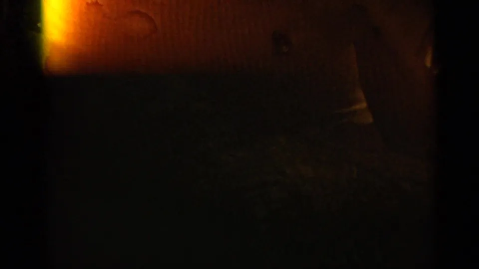 Underexposed 8mm frame with a bright orange flare at left and faint shapes obscured by darkness before the exterior boat view.