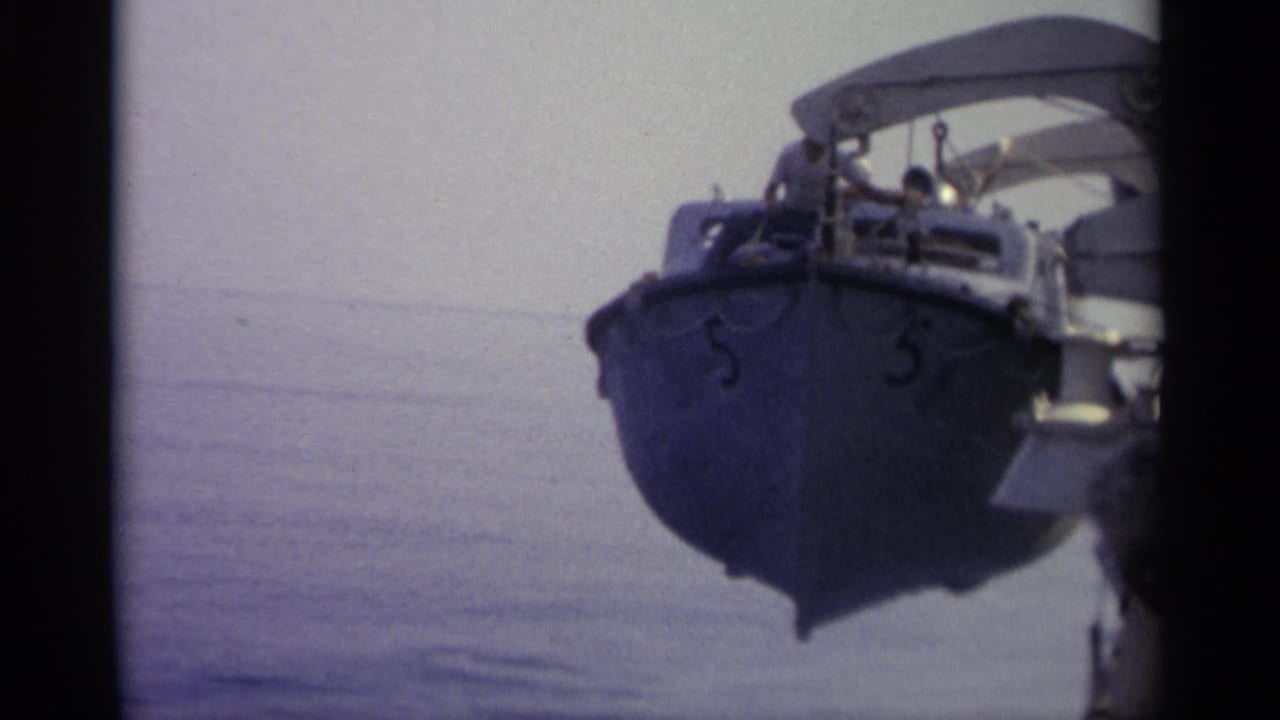 1965 8mm frame showing a small blue boat marked 5 near calm water, with passengers visible beneath a white canopy.