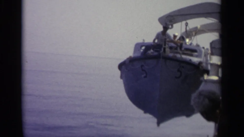 Small blue canopy boat, marked with the number 5, appears alongside calm water in archival 8mm footage from 1965.