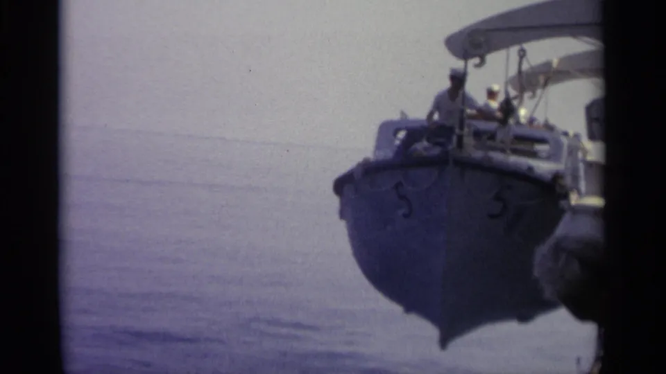 The bow of a blue boat marked 5 fills the frame, with several people aboard and calm open water behind it.