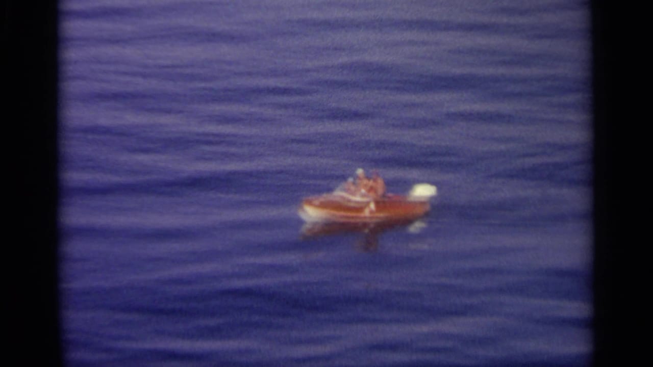 Small red motorboat with two people on calm blue water.