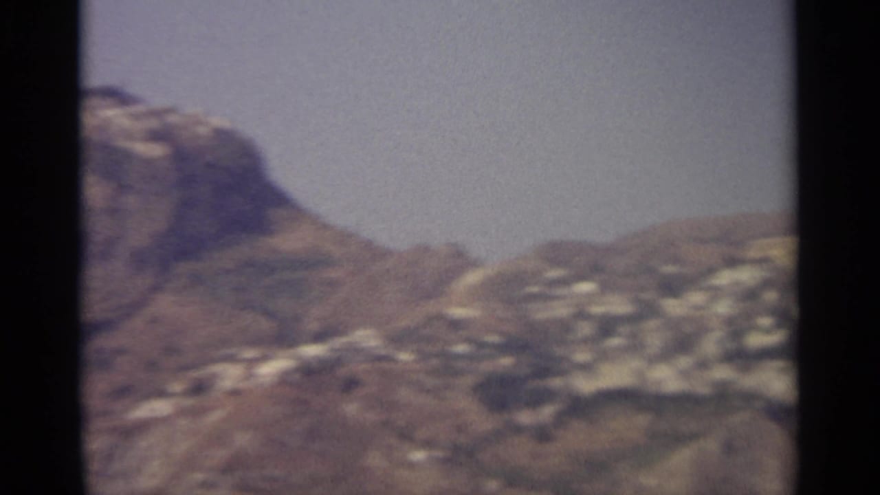 Distant rocky mountain slope with pale hillside buildings under a hazy sky.