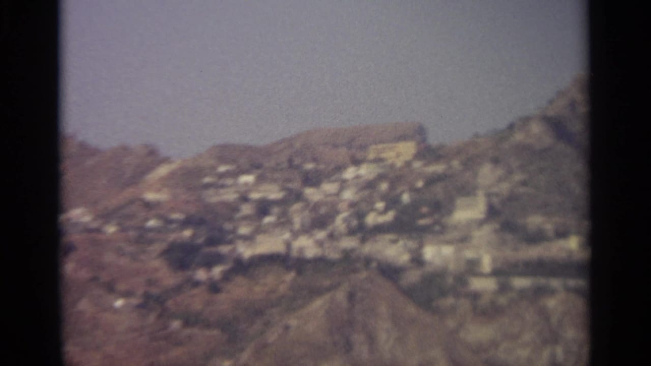 Clustered white buildings on a steep hillside between rocky ridges.