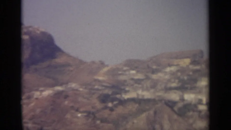 The final frame shows a partial rocky peak, dry slopes, and distant pale buildings on a Sicilian hillside.