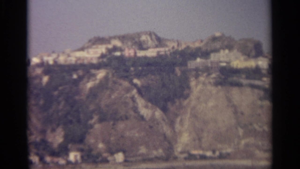 Rocky coastal slope with white buildings and water at the base.