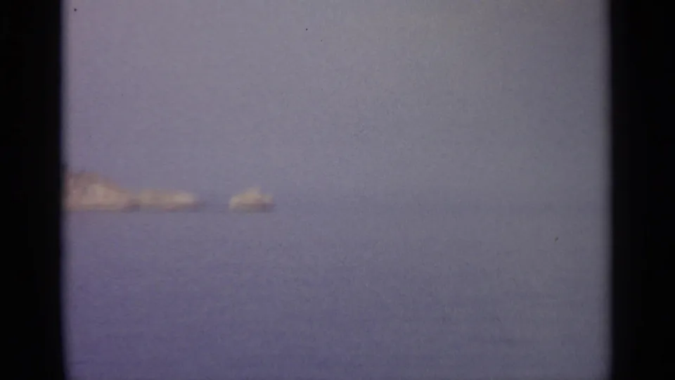 Soft 8mm frame with low rocky forms at the left edge and open water stretching beneath a clear sky.