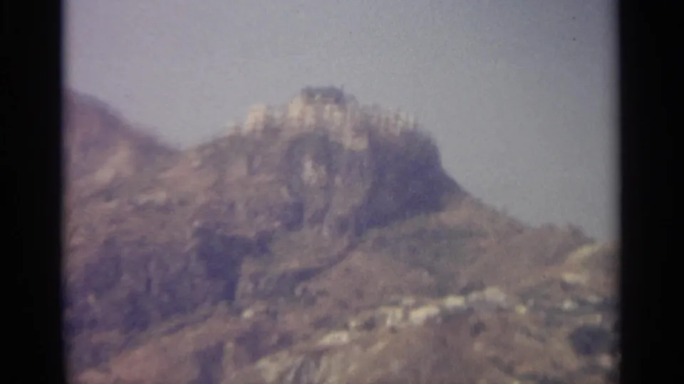 Vintage 8mm view of a rugged Sicilian ridge, with pale buildings or walls clustered near the rocky summit.