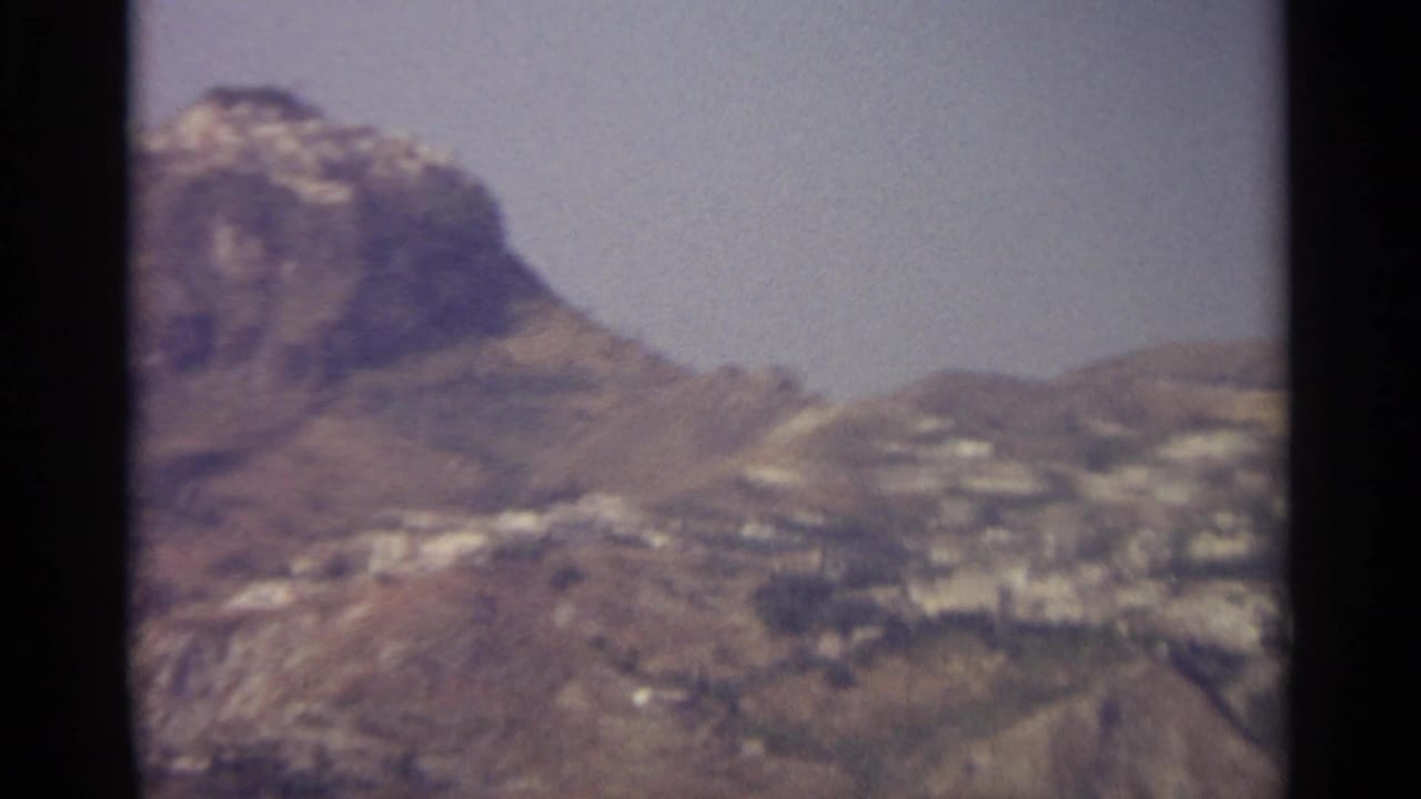 Distant mountain village spread across dry hills beneath a hazy sky.