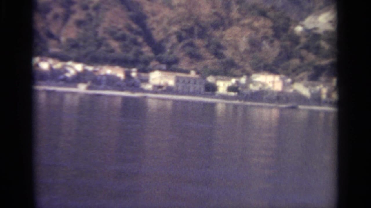 Shoreline buildings and hillside seen across a calm lake through film gate edges.
