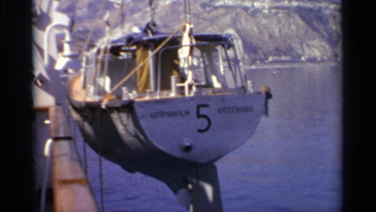 Small sailboat marked Gripsholm and 5 hangs beside a larger vessel over blue water.