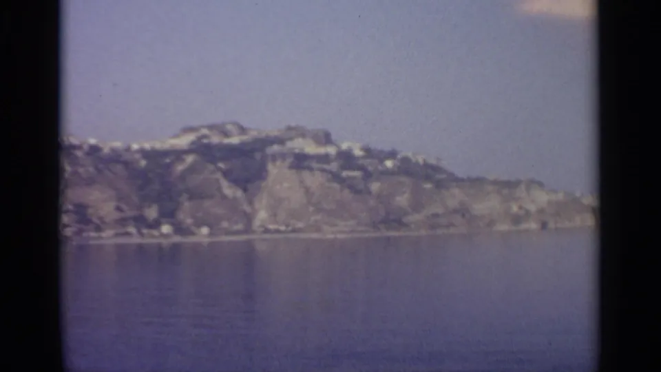 Distant rocky coastline and small shoreline details appear across calm water, framed by dark 8mm film edges.